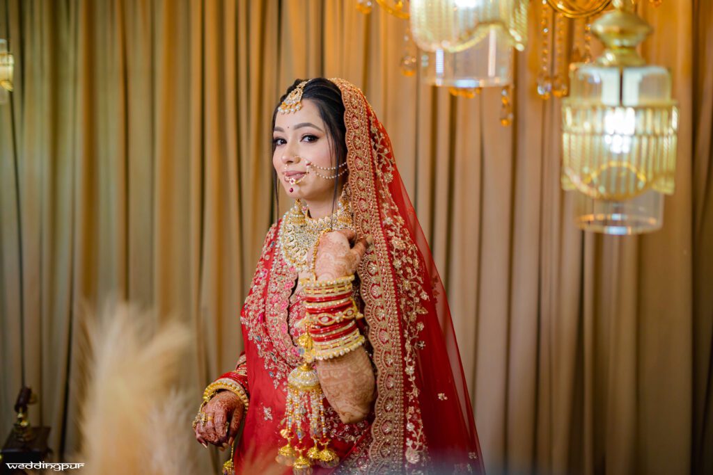Elegant bride posing in red lehenga with jewellery under warm indoor lighting